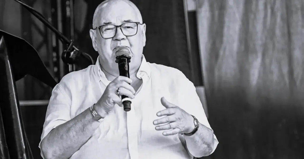 Stanisław Sojka nie żyje. Wokalista w białej koszuli przemawia do mikrofonu, gestykulując.