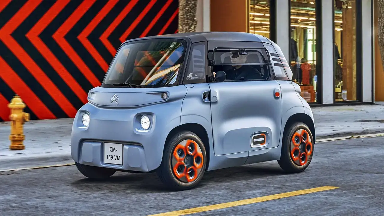 Niebieski Citroën Ami z pomarańczowymi felgami jedzie ulicą.