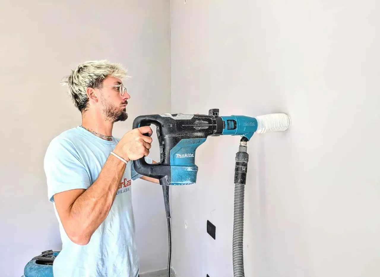 Uomo con trapano Makita che crea un foro nel muro, aspirando la polvere per forare muro senza rovinare intonaco.