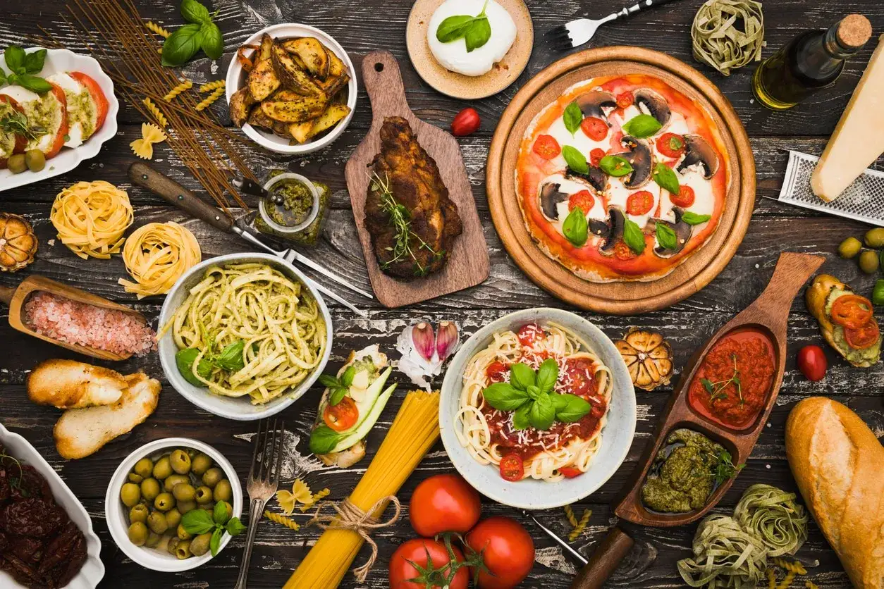 En härlig dukning med italiensk mat: pizza, pasta med pesto och tomatsås, kött, bruschetta och tillbehör.