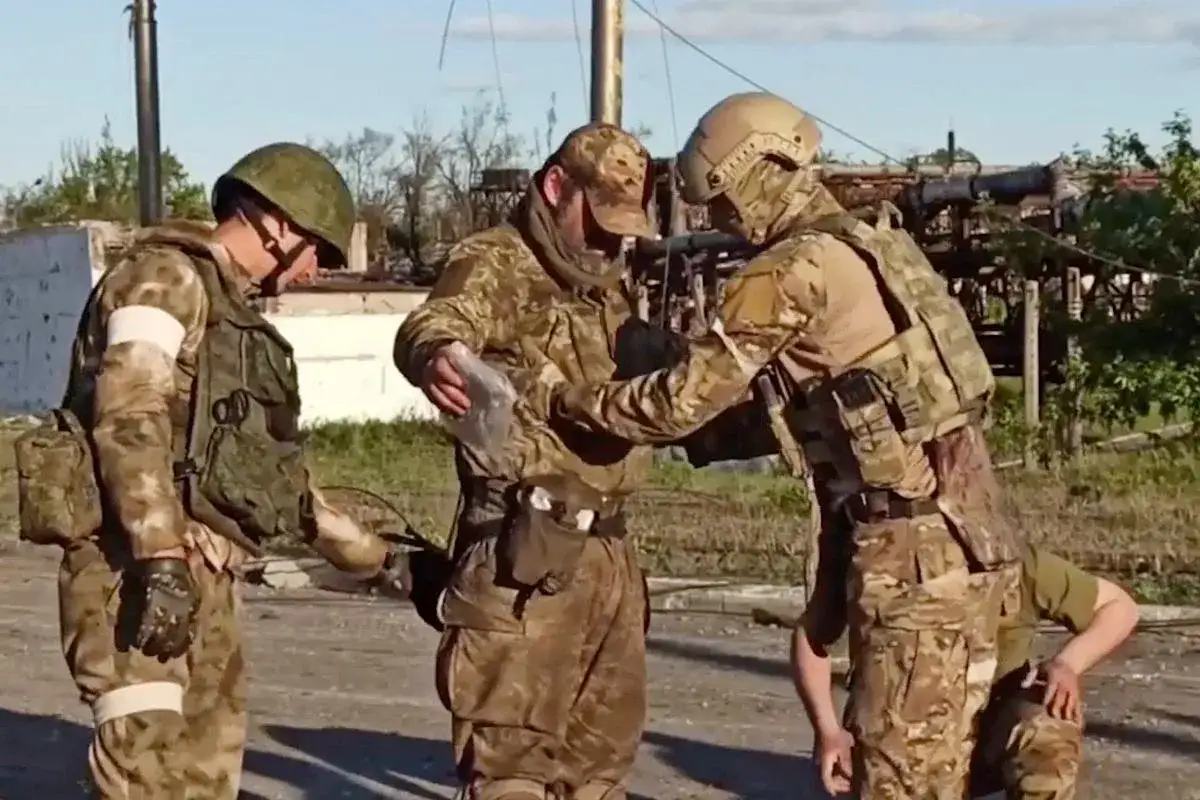Żołnierze w kamuflażu, być może z pułku Azov, wymieniają się czymś w zniszczonym otoczeniu.