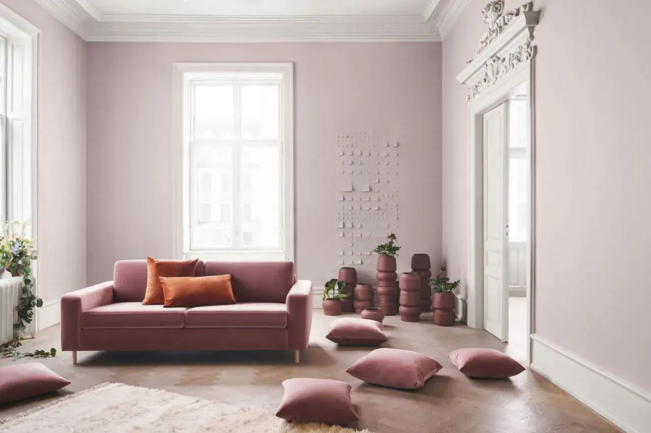 Sanfte rosa Wandfarbe wirkt beruhigend in diesem stilvollen Wohnzimmer mit einem rosafarbenen Sofa und vielen Kissen.
