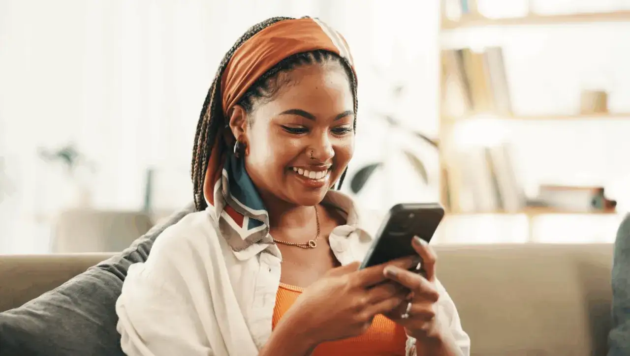 Une jeune femme souriante regarde son t&eacute;l&eacute;phone, peut-&ecirc;tre en attendant qu'il ne r&eacute;pond pas &agrave; mon message.
