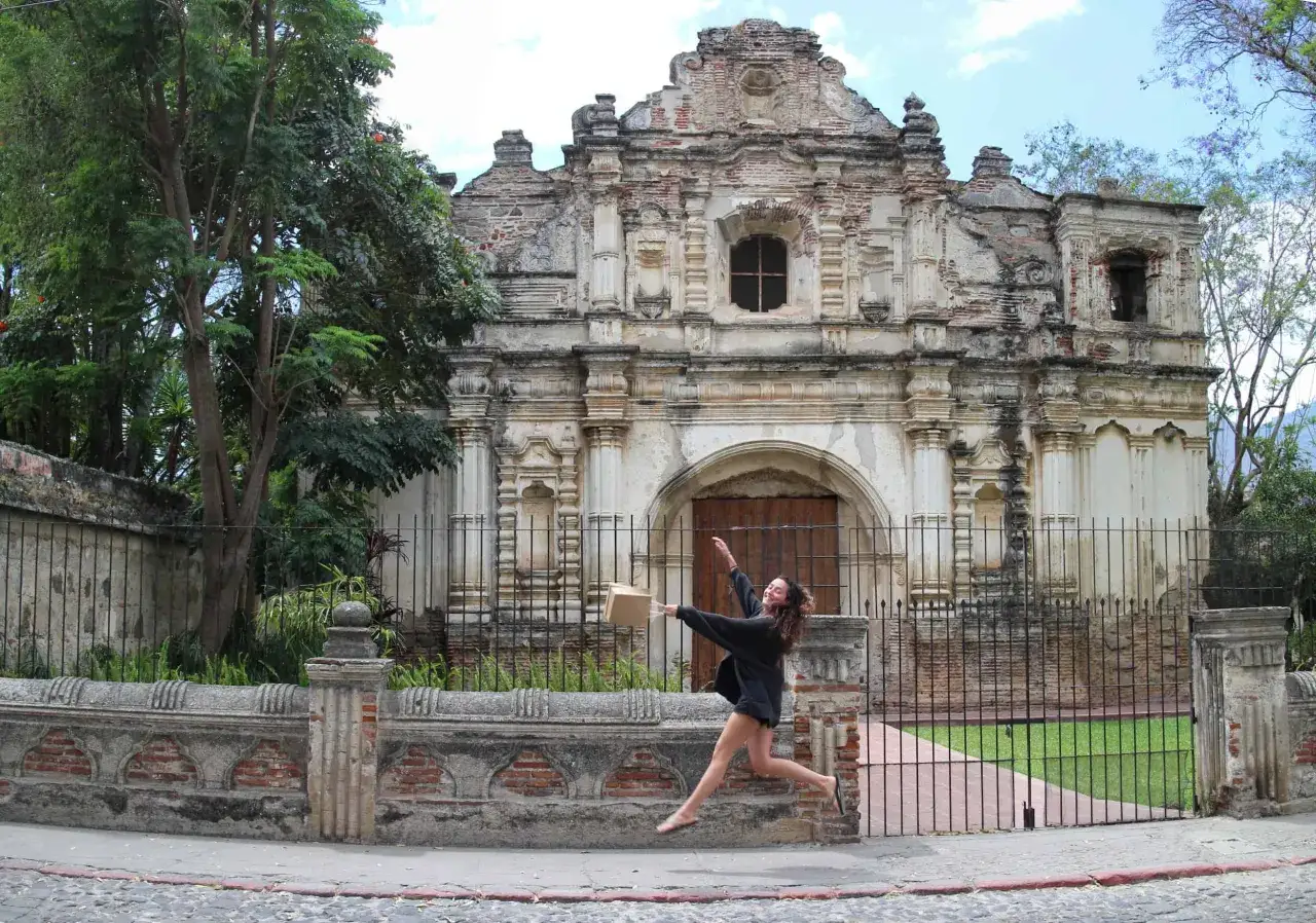 Una joven salta de alegría frente a las ruinas de una iglesia colonial, un sitio imperdible que ver en Antigua Guatemala.