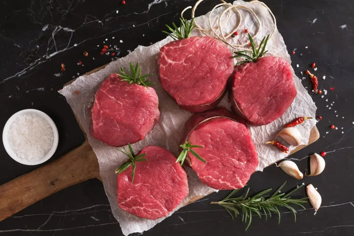 Pięć soczystych steków z polędwicy wołowej, udekorowanych rozmarynem, czosnkiem i papryczkami chili, gotowych do grillowania.