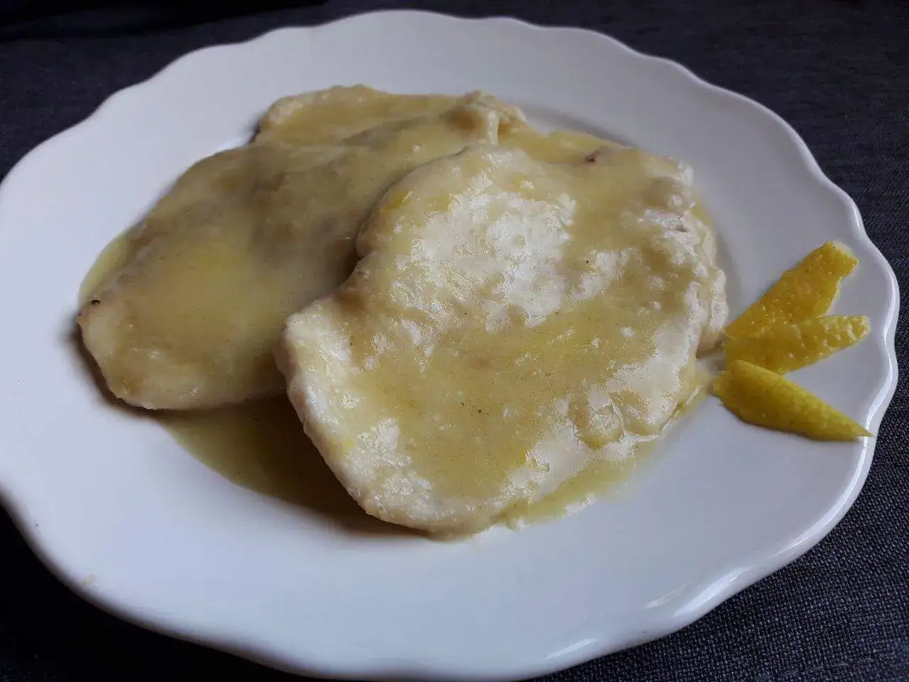 Petto di pollo al limone cremoso, servito su un piatto bianco con scorze di limone.