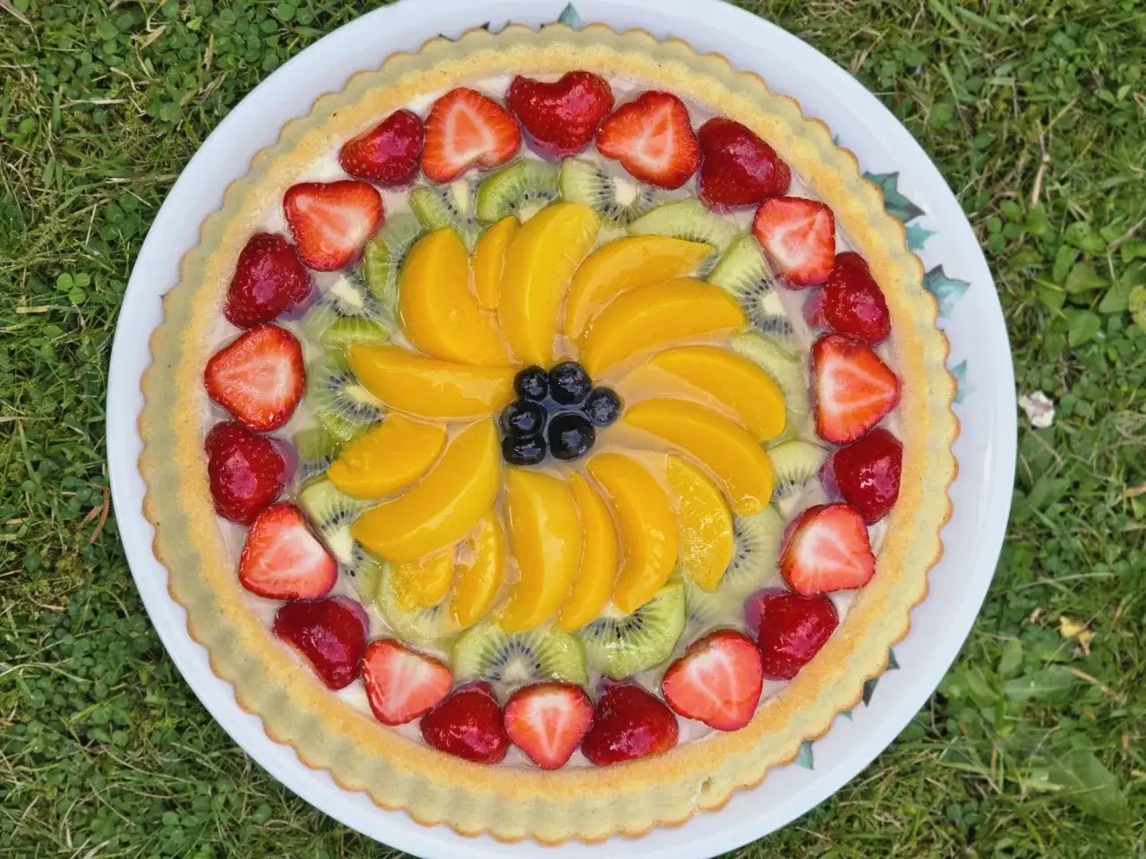 Tarte aux fruits color&eacute;e sur une base de cr&egrave;me patissi&egrave;re. Fraises, kiwis, p&ecirc;ches et myrtilles forment un motif floral.