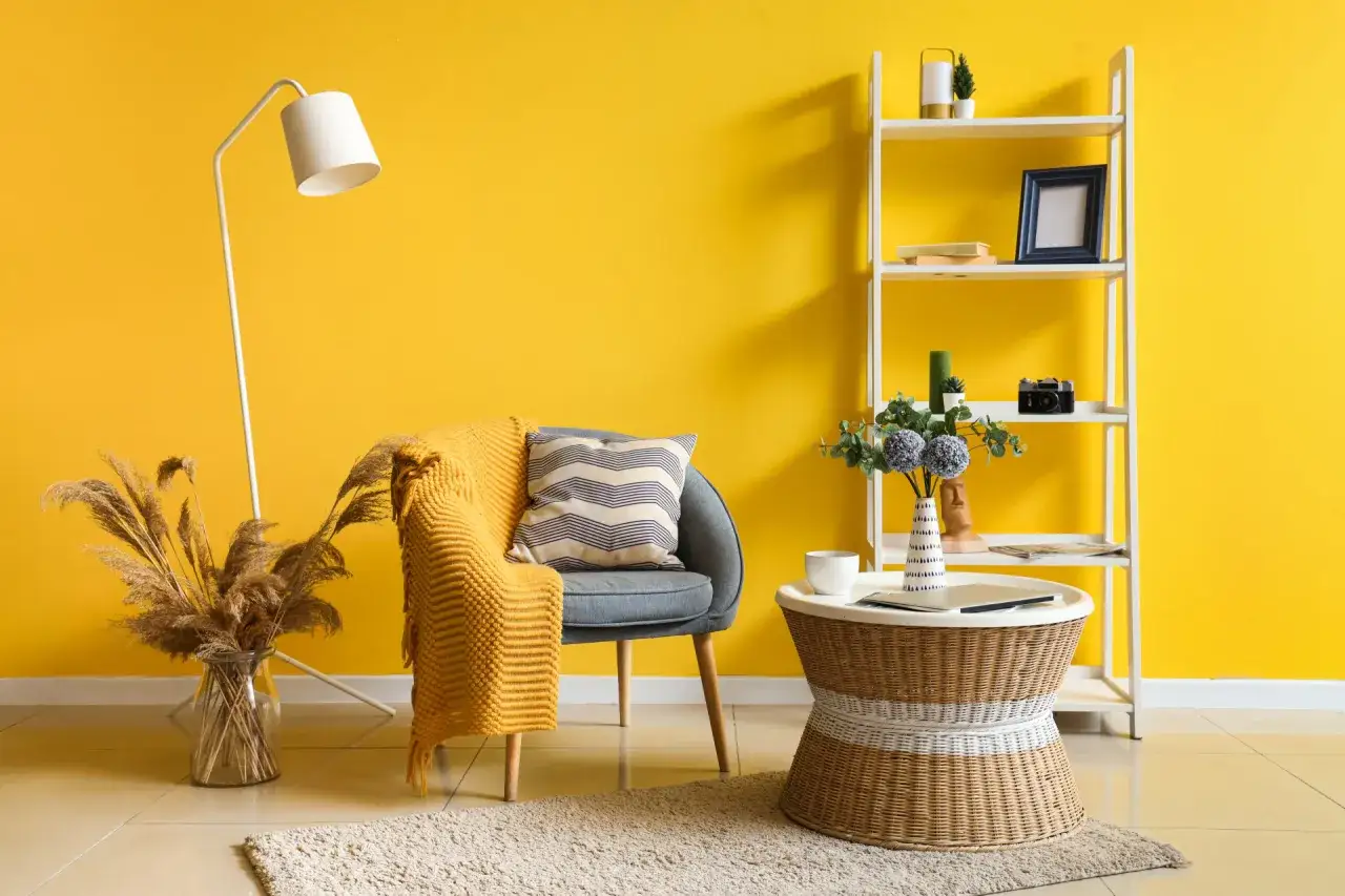 Un fauteuil confortable avec une couverture jaune vif, un lampadaire et une &eacute;tag&egrave;re blanche sur un mur jaune &eacute;clatant.