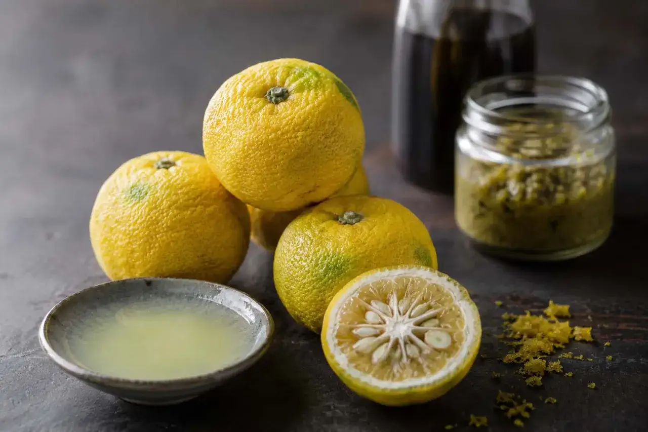 Yuzu que es: cítricos amarillos, jugo en un cuenco, y una pasta verde en un frasco.