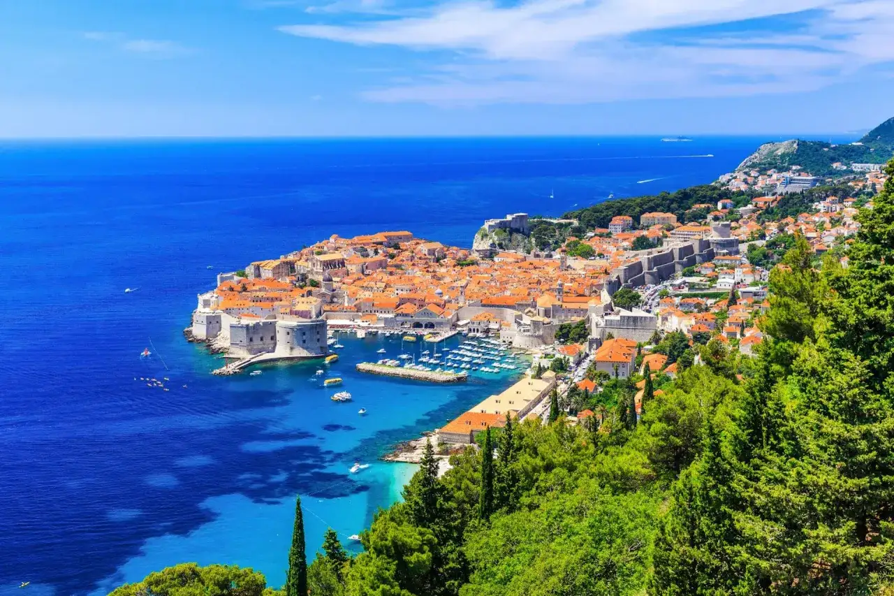 Vacker vy &ouml;ver gamla stan Dubrovnik med sina orangea tak och stadsmurar som m&ouml;ter det turkosbl&aring; havet. En idyllisk bild av Kroatiens p&auml;rla.