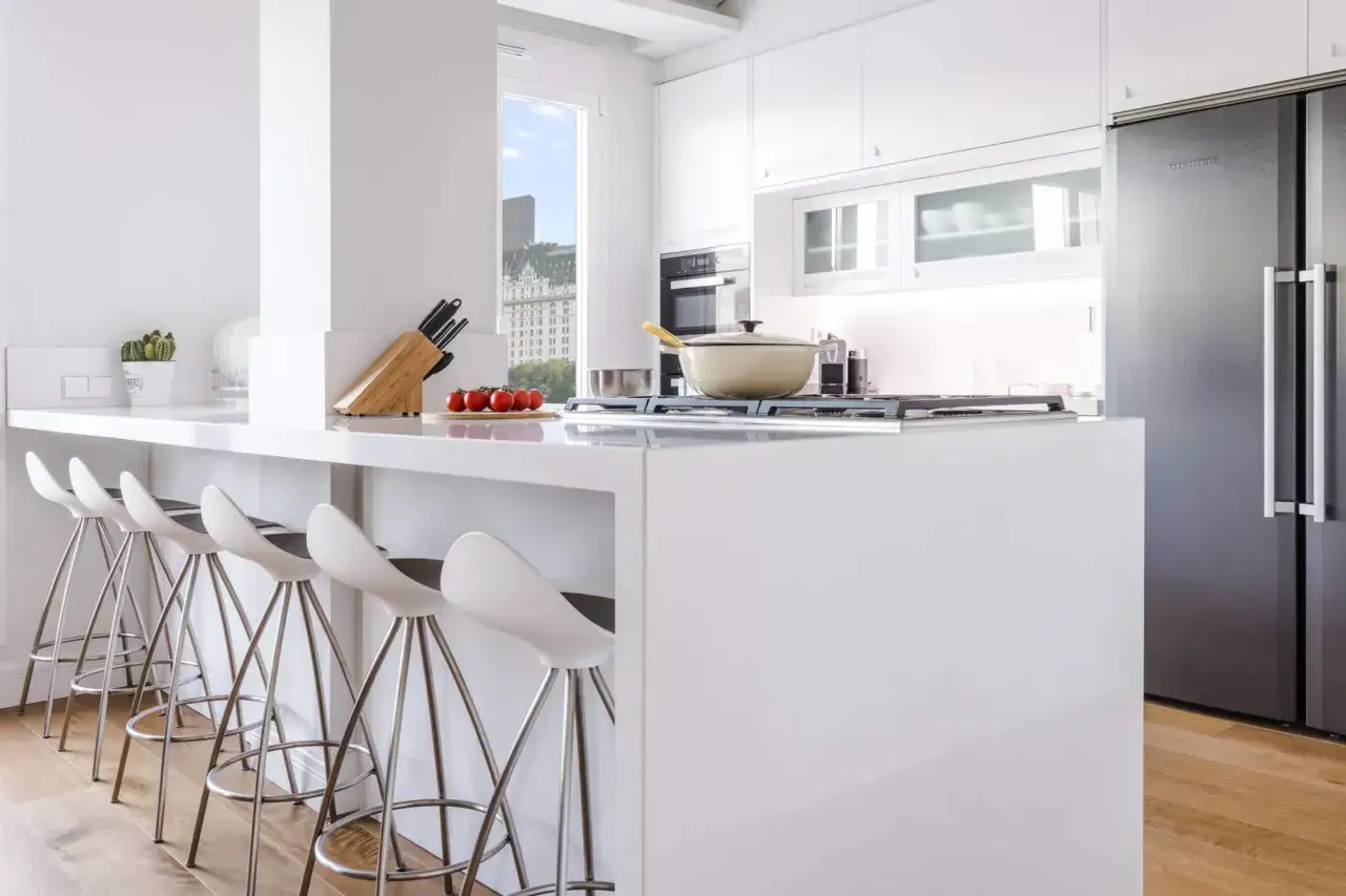 Moderna cocina office blanca con barra, taburetes, electrodomésticos y vista urbana.