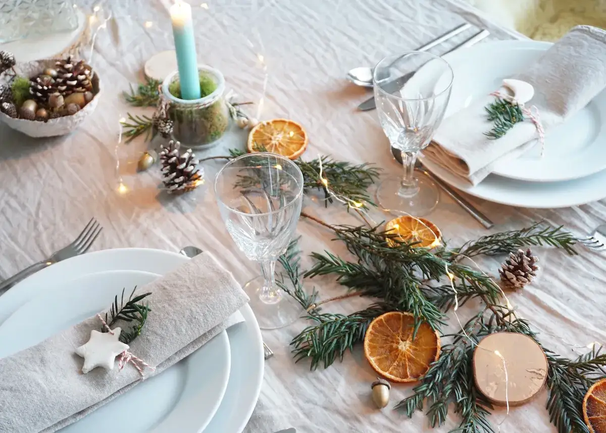 Déco table Noël nature à faire soi même : guirlande de sapin, oranges séchées, pommes de pin, bougie et étoiles en pâte à sel.