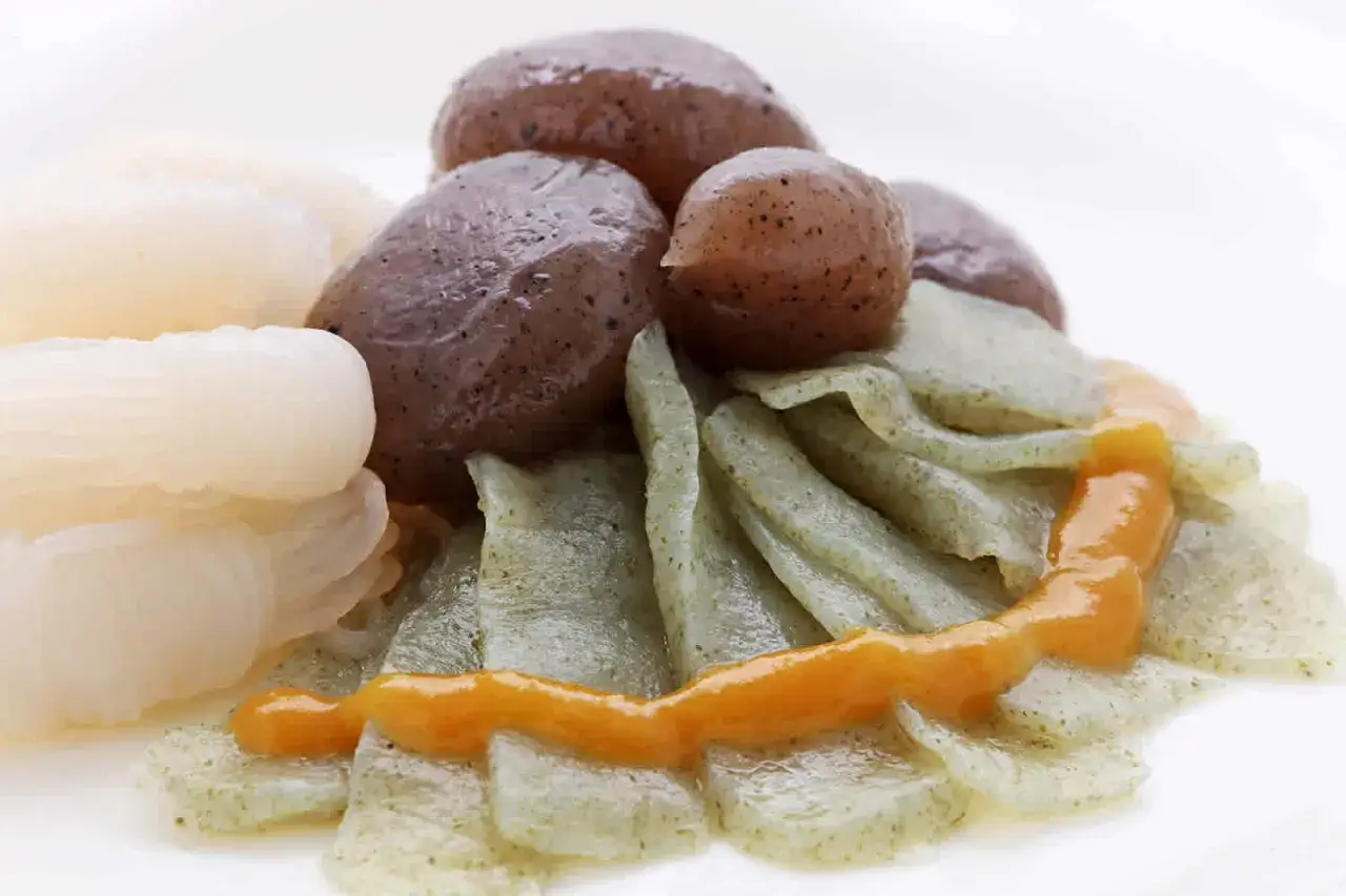 Oto danie z konjac: białe, podłużne kawałki, brązowe kulki i zielone, płaskie paski, polane pomarańczowym sosem. Konjac co to? To zdrowy składnik.