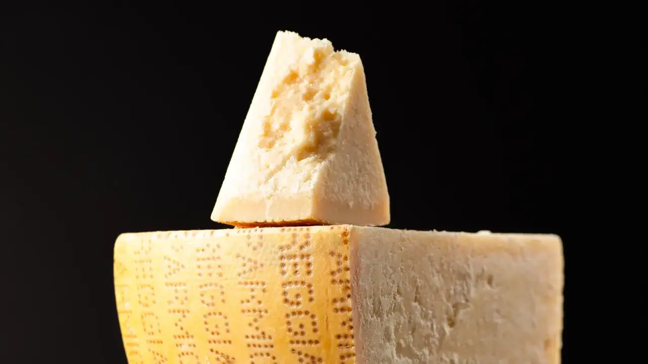Ein Stück Parmigiano Reggiano, der berühmte Parmesan, liegt auf einem größeren Stück desselben Käses.