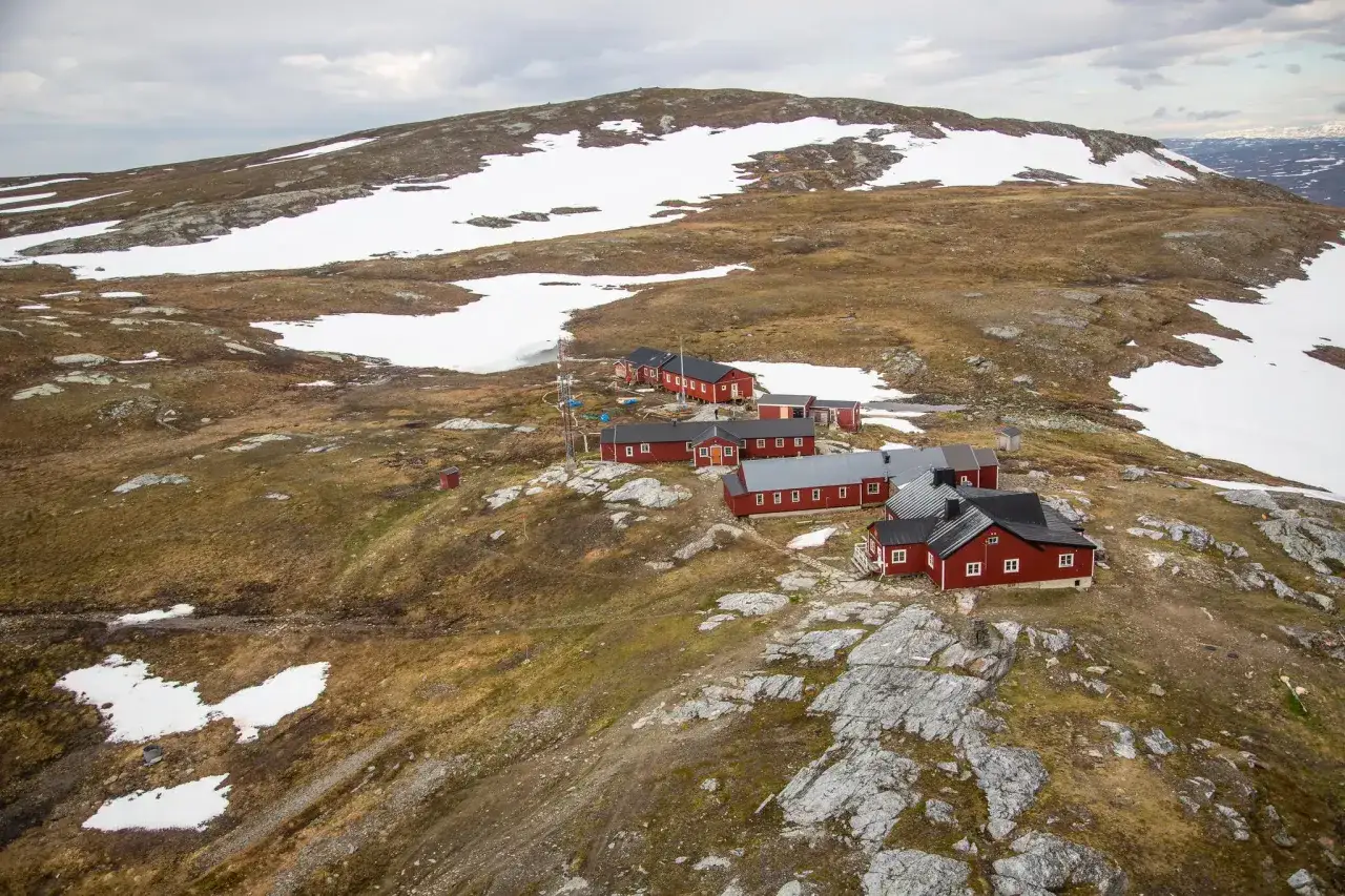 STF Blåhammaren fjällstation, en samling röda hus med vita knutar, ligger utspridd i ett snöigt och kargt fjällandskap.