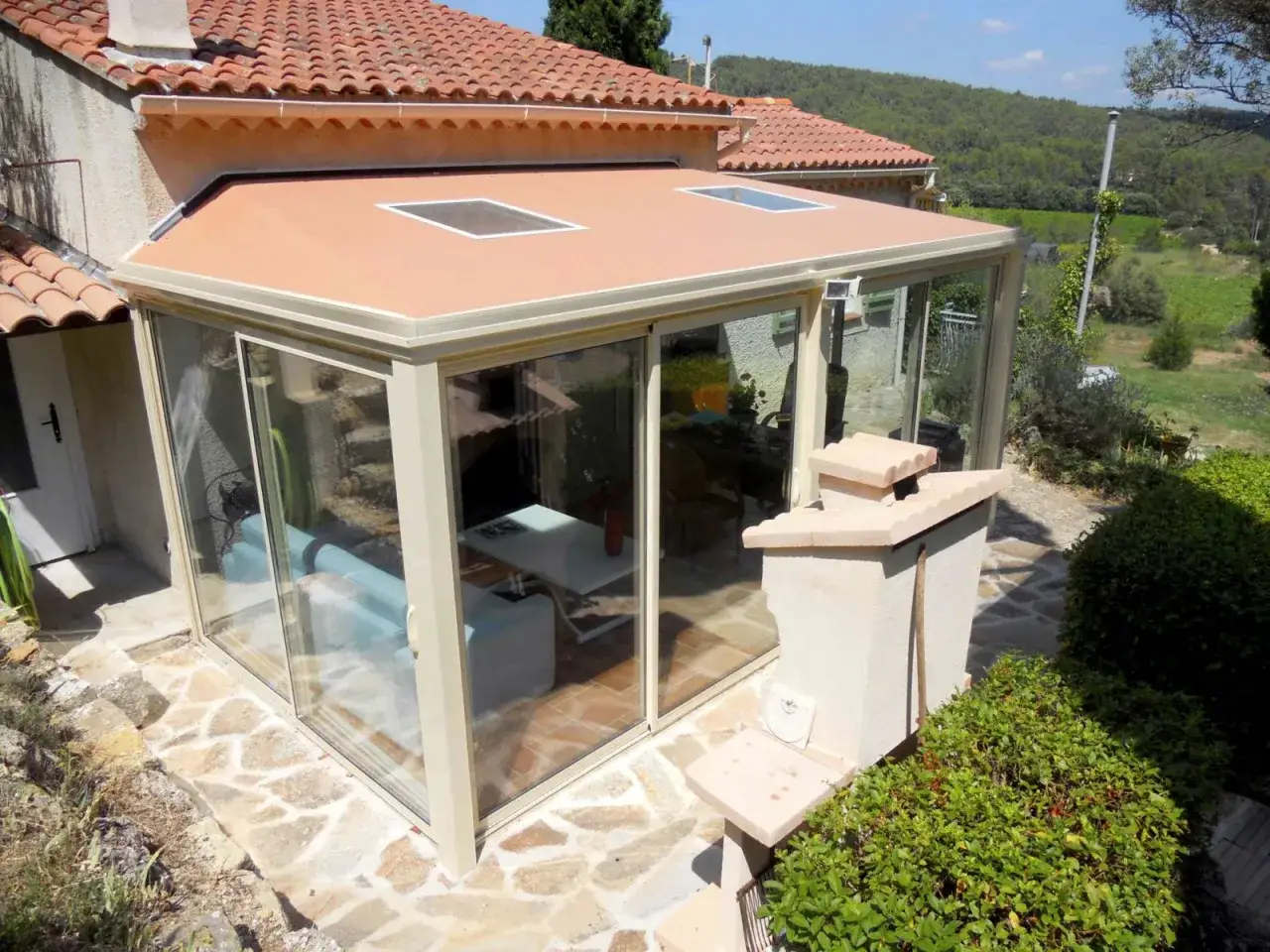 Une **veranda tuile** moderne avec de grandes baies vitr&eacute;es et deux puits de lumi&egrave;re, offrant une vue sur un paysage verdoyant.