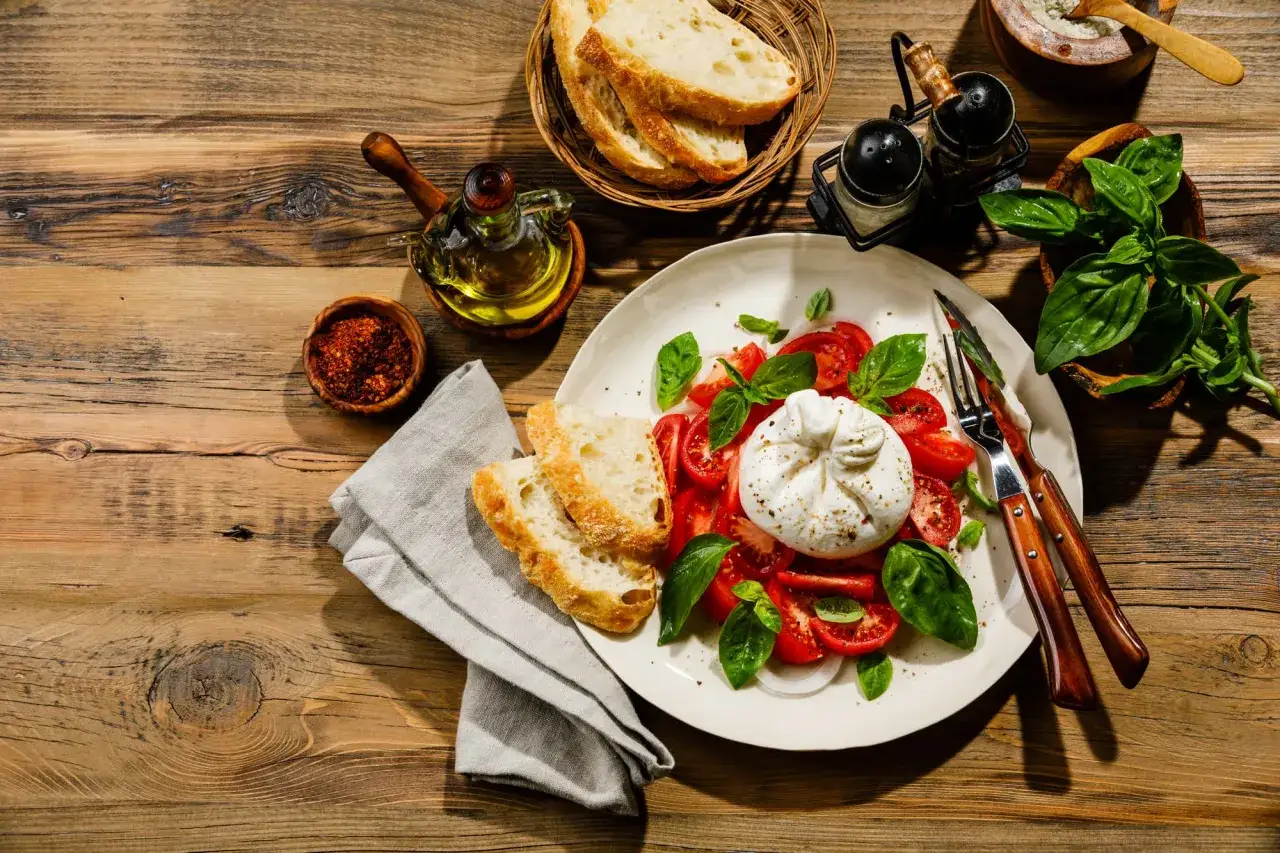 Une assiette de tomates, de basilic et de la burrata crémeuse, accompagnée de pain croustillant et d'huile d'olive.