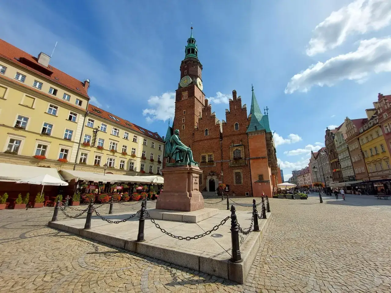 Das historische Rathaus und die bunten H&auml;user pr&auml;gen das lebendige **Wrocław centrum**. Eine Statue steht im Vordergrund auf dem gepflasterten Platz.