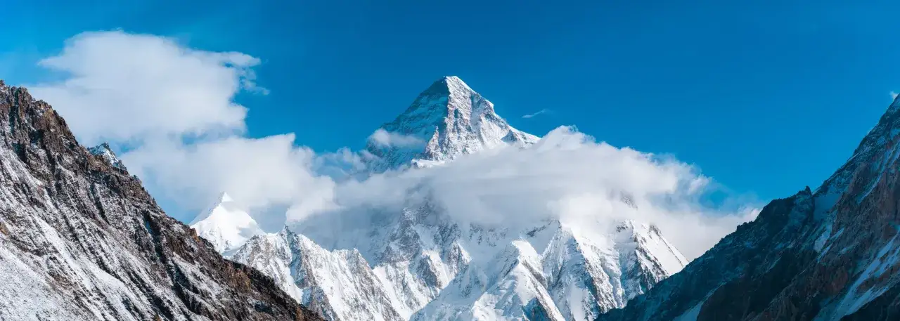 Majestatyczny, ośnieżony K2, najwyższy szczyt Karakorum, wyłania się z chmur na tle błękitnego nieba.