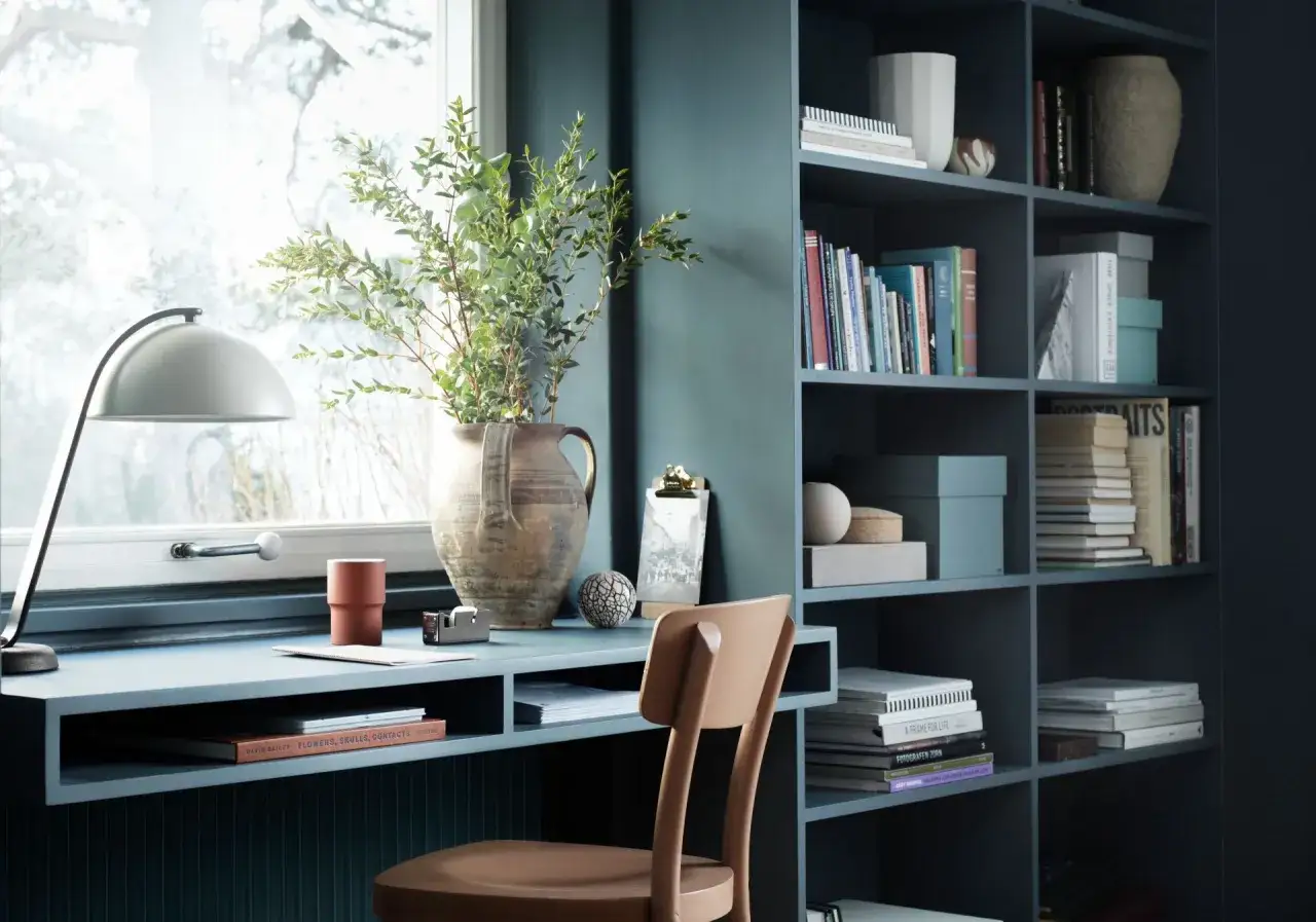 En mysig arbetsplats med ett blått skrivbord, en lampa och en bokhylla fylld med böcker. Kanske dags att måla om skrivbordet i en ny färg?