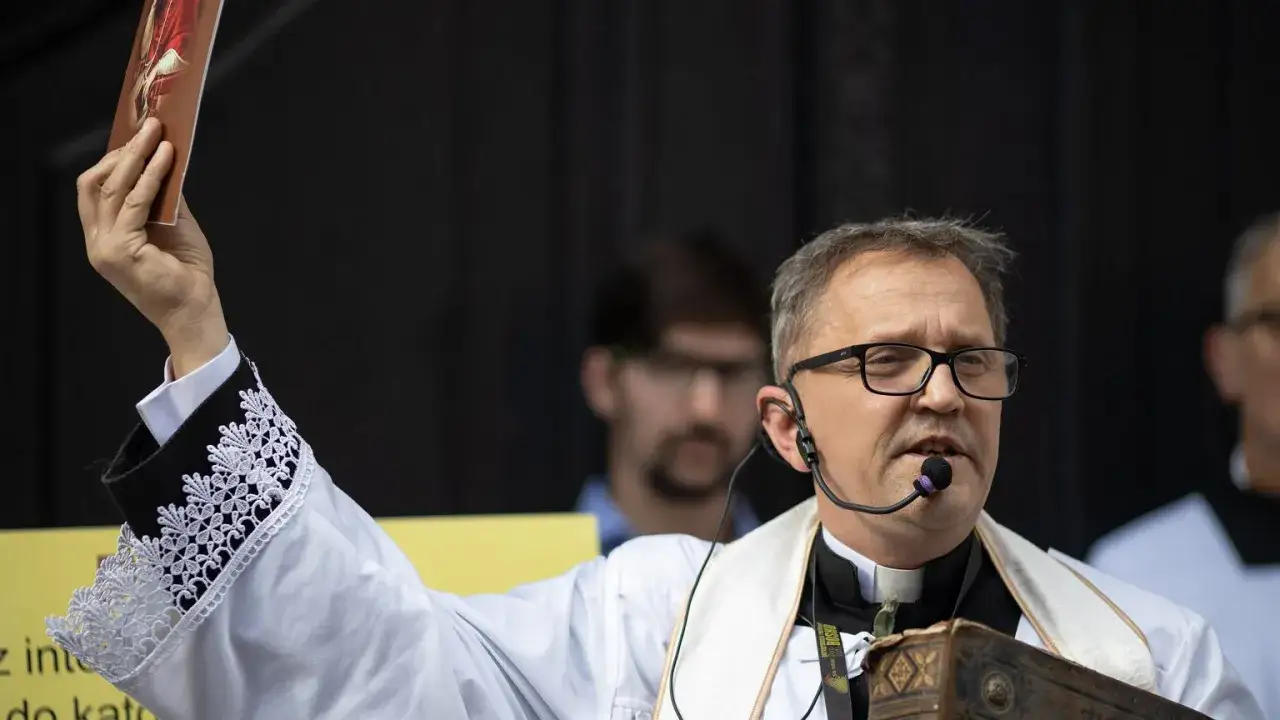 Ksiądz Michał Woźnicki w białej albie z koronkowymi mankietami podnosi obrazek.