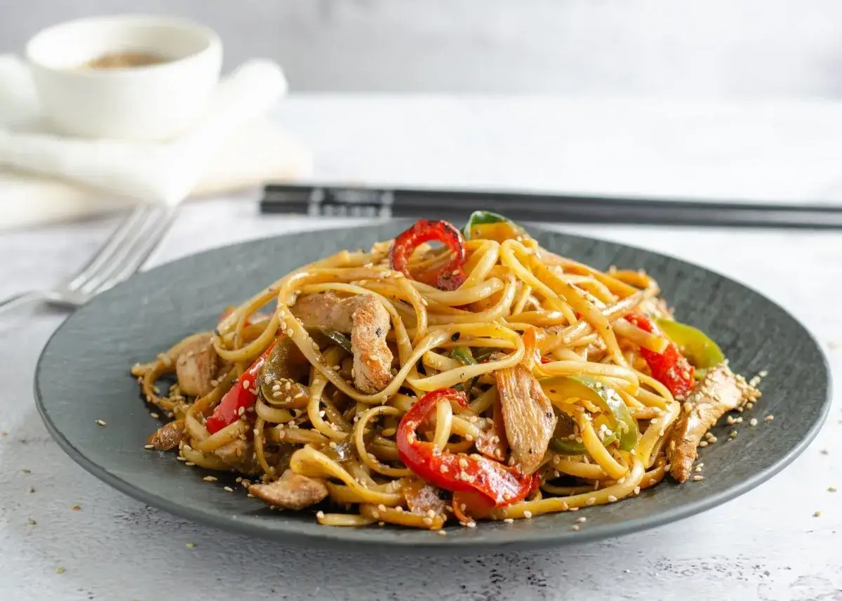 Un plato de deliciosos noodles con pollo, pimientos rojos y verdes, y semillas de sésamo.