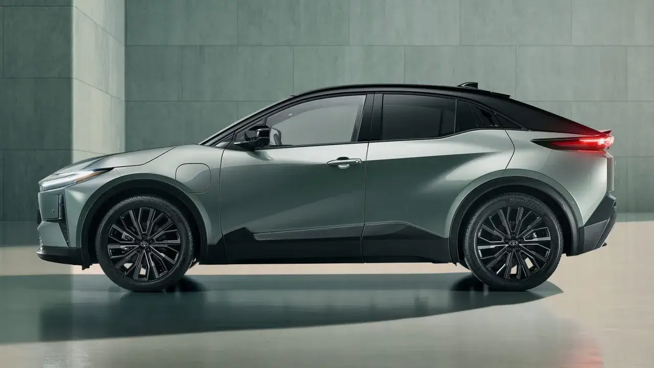 En grönmetallic Toyota C-HR+ med svart tak står parkerad framför en modern betongvägg.