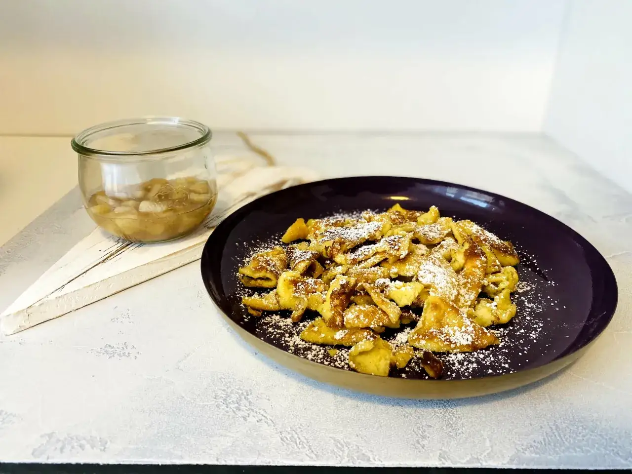 Kaiserschmarrn, fluffig und goldbraun, mit Puderzucker bestäubt, daneben Apfelmus im Glas. So einfach gelingt er mit dem Thermomix.