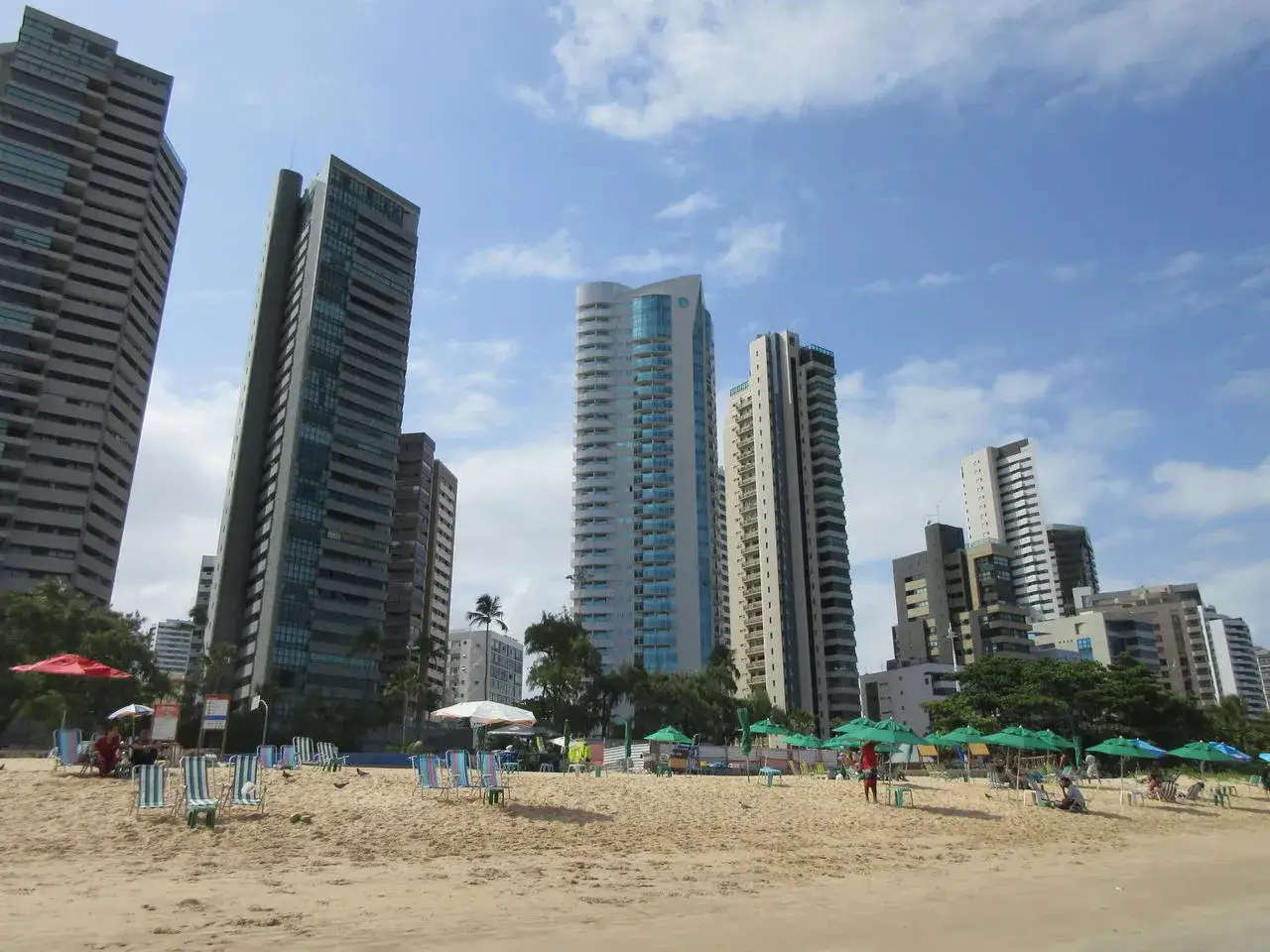 Hohe Geb&auml;ude ragen &uuml;ber den Sandstrand von Recife, Brasilien, auf, wo Liegest&uuml;hle und Sonnenschirme auf Besucher warten.