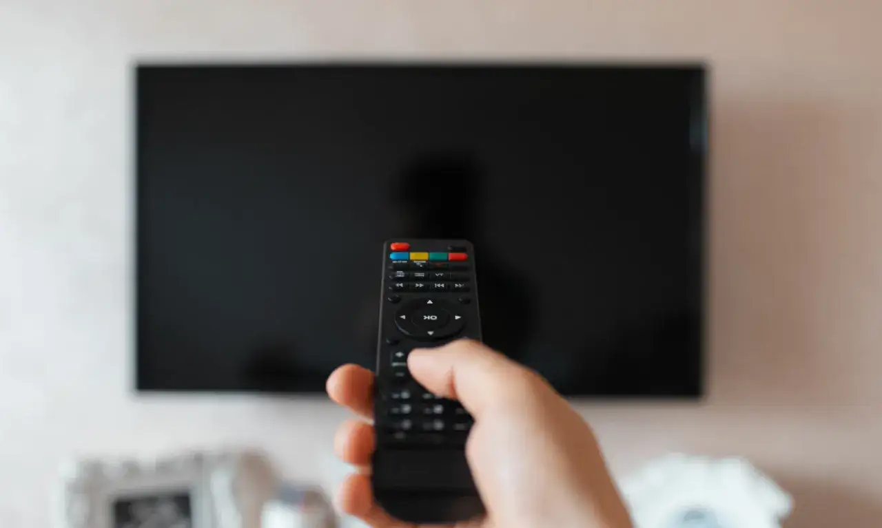 Dłoń trzymająca pilot przed wyłączonym telewizorem. Czy syndyk może zabrać telewizor? To pytanie nurtuje wiele os&oacute;b.