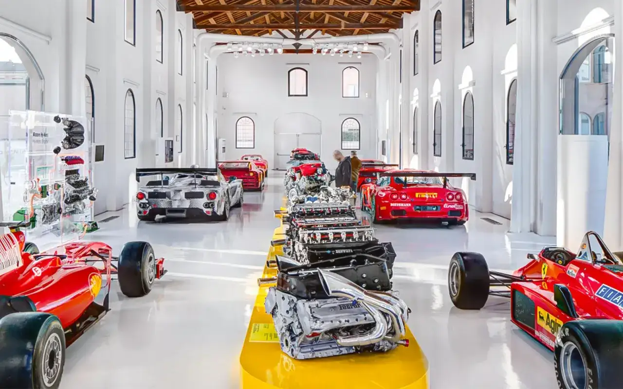 Wnętrze muzeum Ferrari w Maranello lub Modenie. Widać bolidy F1, silniki i samochody wyścigowe.