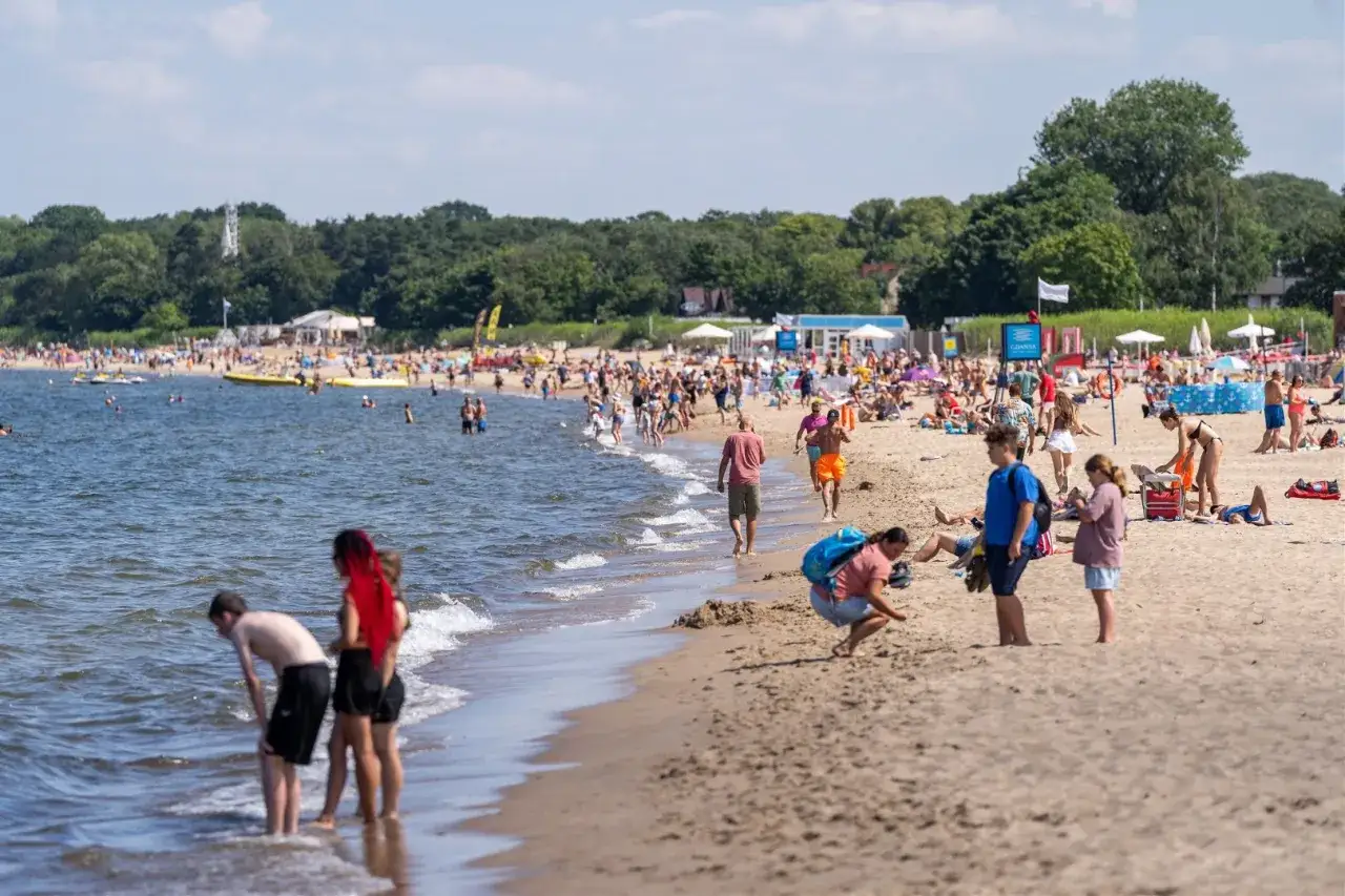 Tłum ludzi na plaży, szukający odpowiedzi, gdzie najszybciej nad morze z Poznania. Słońce, woda i piasek.