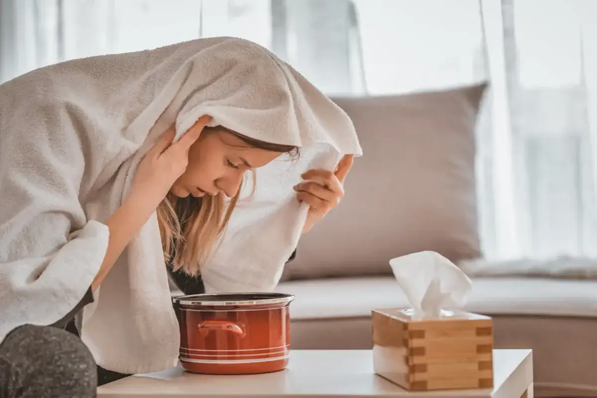 Une femme apprend comment faire une inhalation, la tête couverte d'une serviette au-dessus d'une casserole de vapeur.