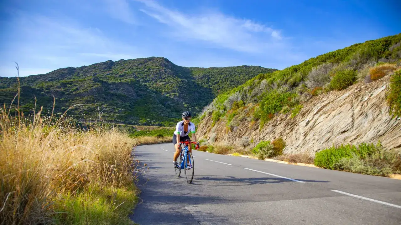 Rennradfahrerin auf Korsika genie&szlig;t die bergige Landschaft unter blauem Himmel.