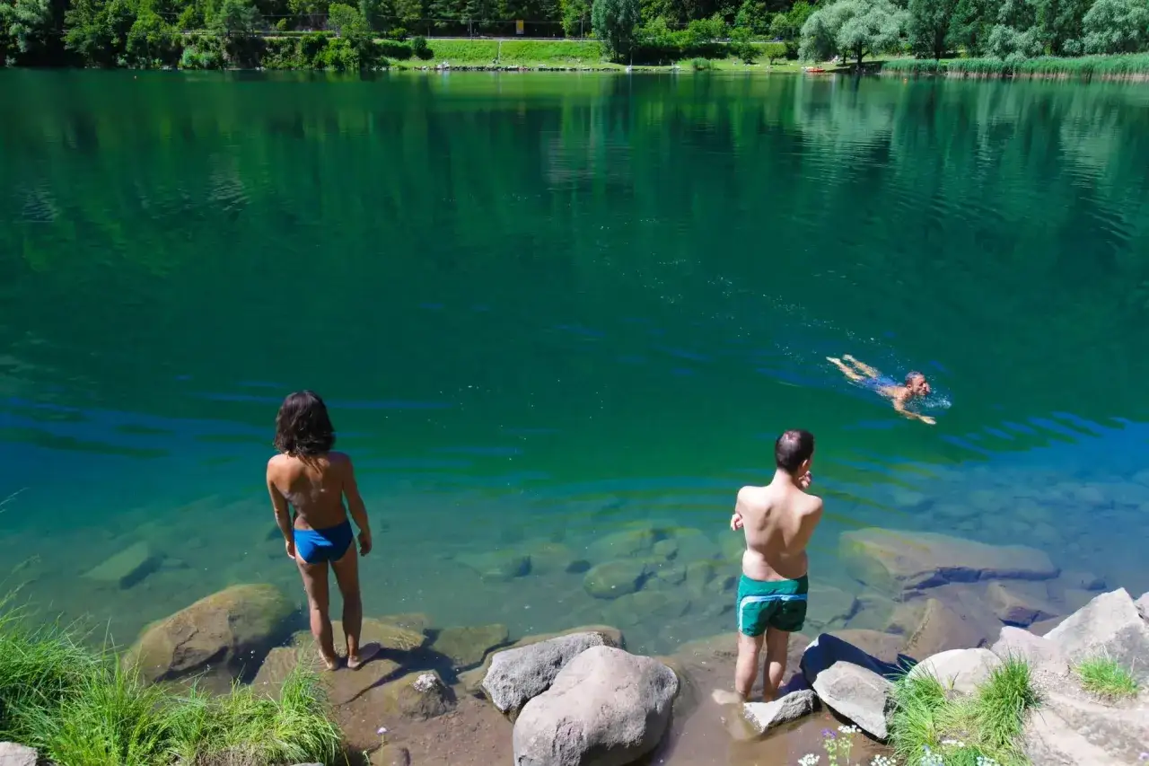 Coppia al **lago di Lases**, uno nuota, l'altra osserva le acque cristalline.