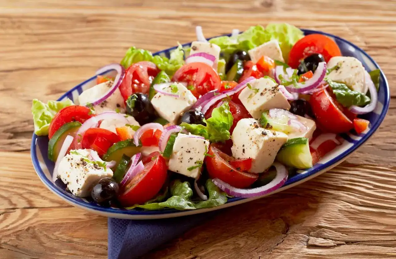 En fräsch grekisk sallad med tomater, gurka, rödlök, oliver och fetaost på en blåvit tallrik.