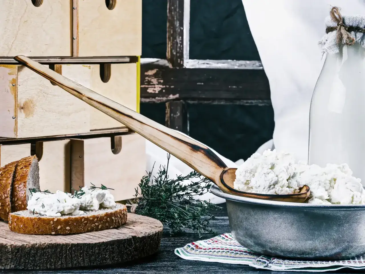 Fromage blanc frais, parfait pour une recette fromage blanc yaourtière. Servi sur du pain avec des herbes, à côté d'une bouteille de lait.