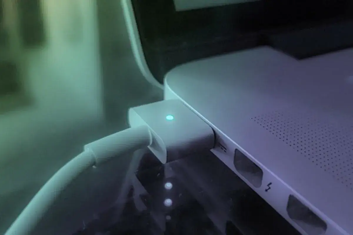 Ładowarka podłączona do laptopa z zapaloną niebieską diodą.