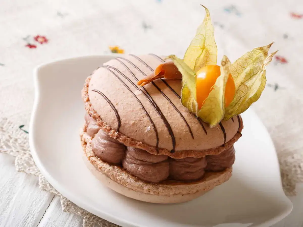 Un macaron chocolat au lait, garni de crème onctueuse et décoré d'une physalis, prêt à être dégusté.