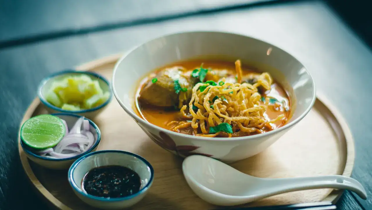 Aromaticzne danie z makaronem, które może być ramen lub udon, podane z dodatkami: limonką, cebulą i pikantnym sosem.