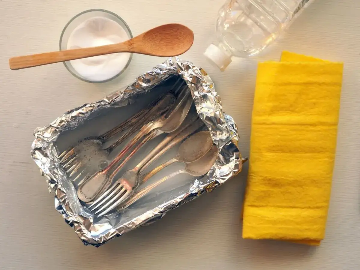 Czyszczenie sztućców sodą: folia aluminiowa, soda, woda i żółta ściereczka.