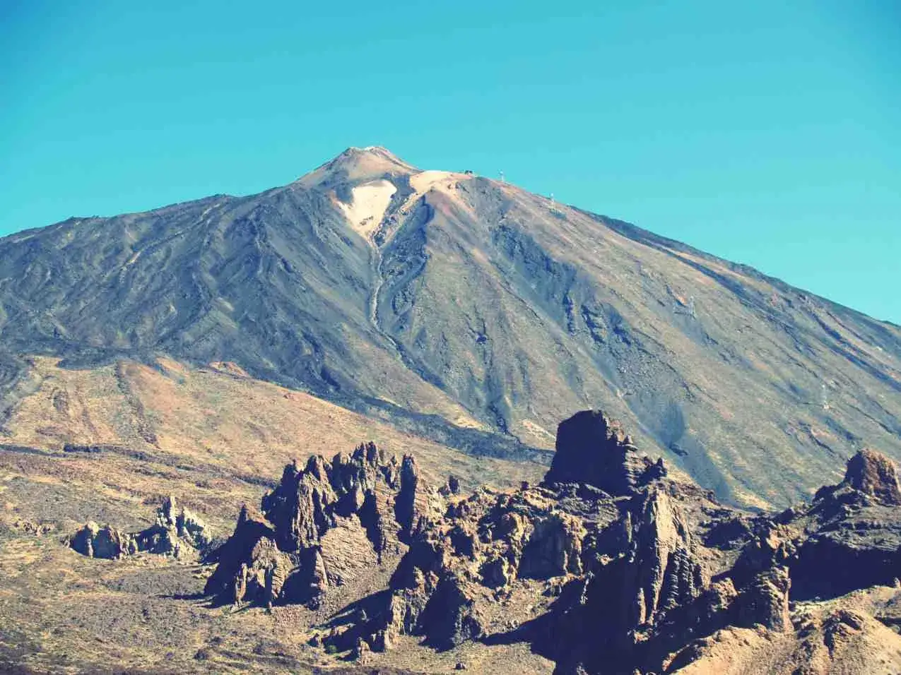 Vulkan Pico del Teide mit felsiger Landschaft im Vordergrund und blauem Himmel.
