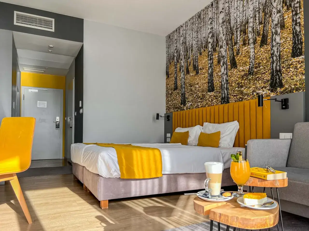 Pokój hotelowy z motywem lasu, żółtym akcentem i napojami. Idealne miejsce na relaks, jak sugerują notera hotel spa opinie.
