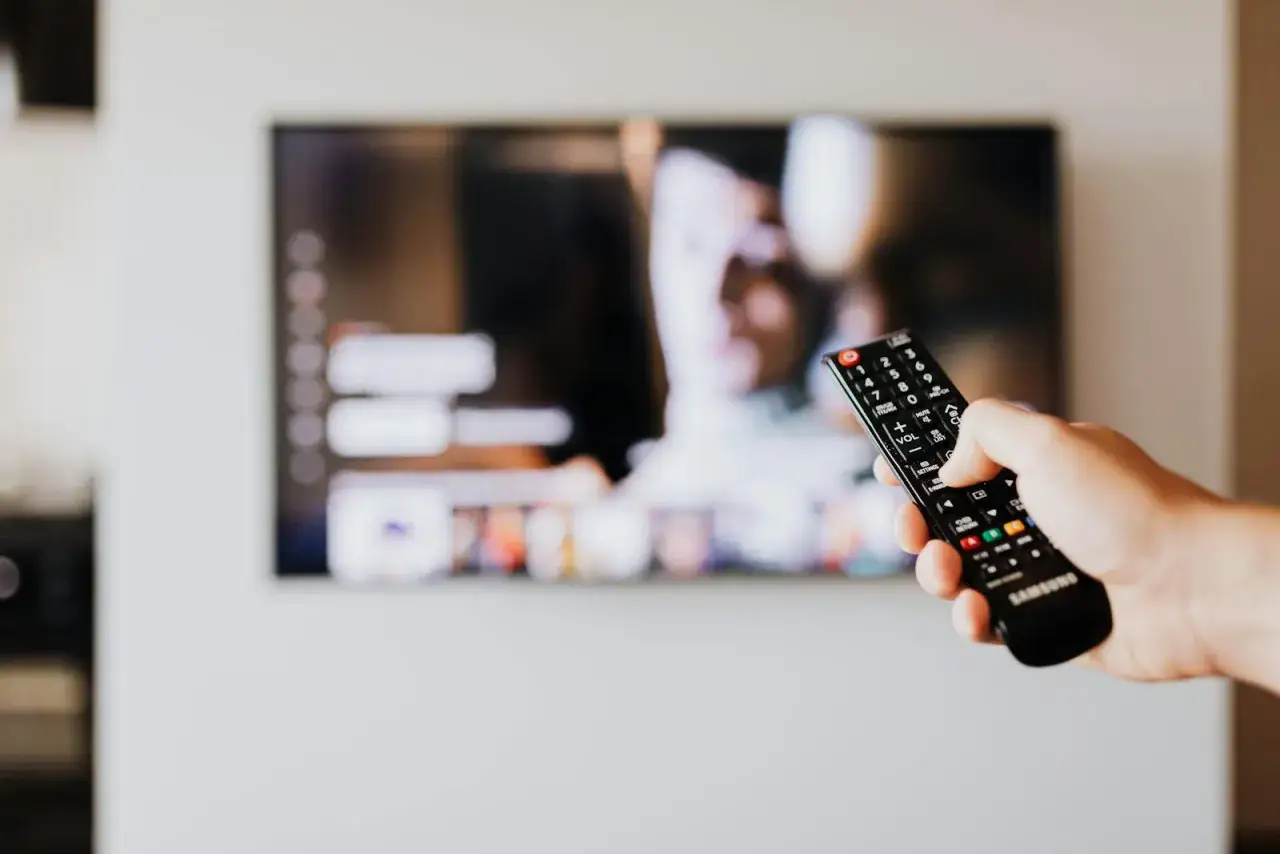 Dłoń trzymająca pilot do telewizora LG na tle wyłączonego ekranu.