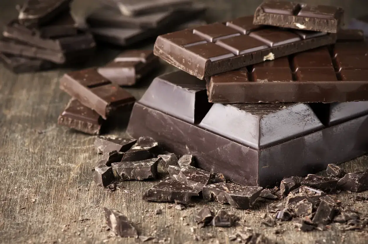 Des morceaux de chocolat noir, entiers et brisés, sur une table en bois. Une invitation à découvrir comment adoucir le chocolat noir pour une dégustation parfaite.