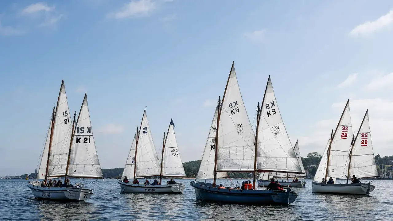 Segelboote mit weißen Segeln und Nummern wie "21" und "K9" auf dem Wasser, ein Teil der Veranstaltung "wm kiel".