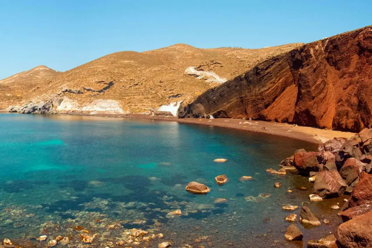 Santorini plaże: Czerwona plaża z turkusową wodą i skalistymi klifami.
