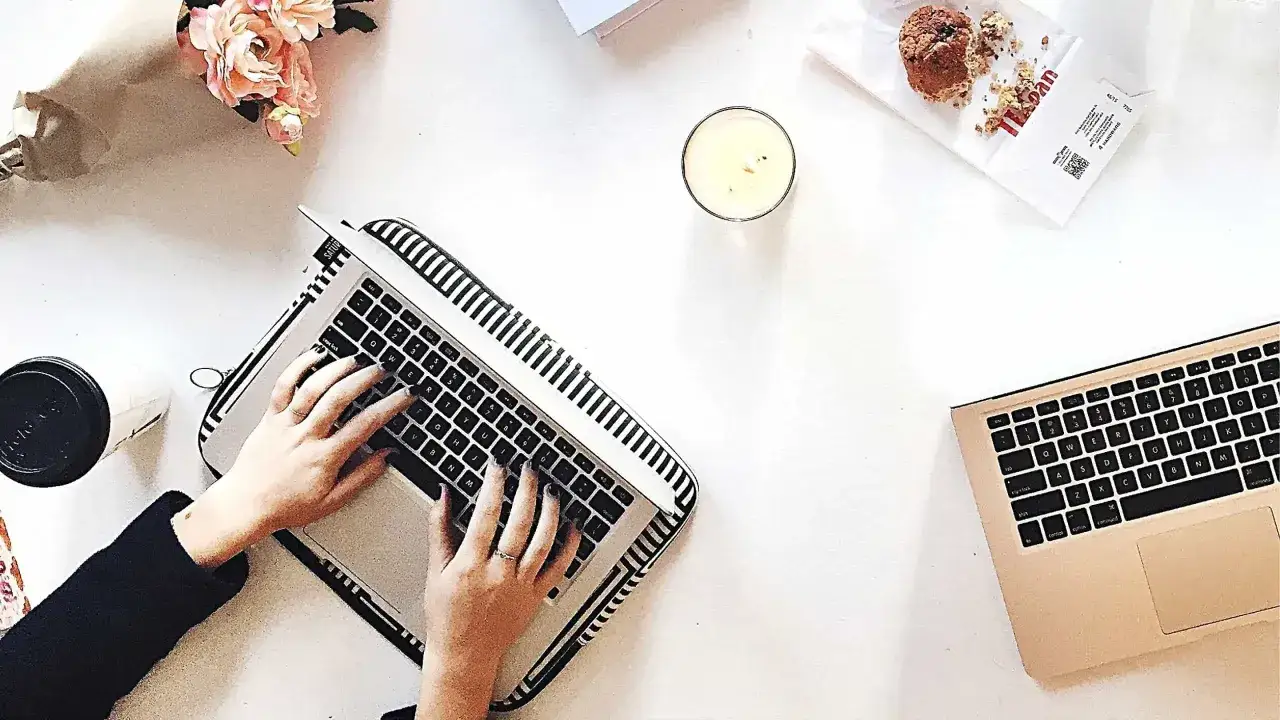 Kobieta pisze na laptopie, przygotowując wypowiedzenie umowy o dzieło. Obok świeca, muffinka i bukiet kwiatów.