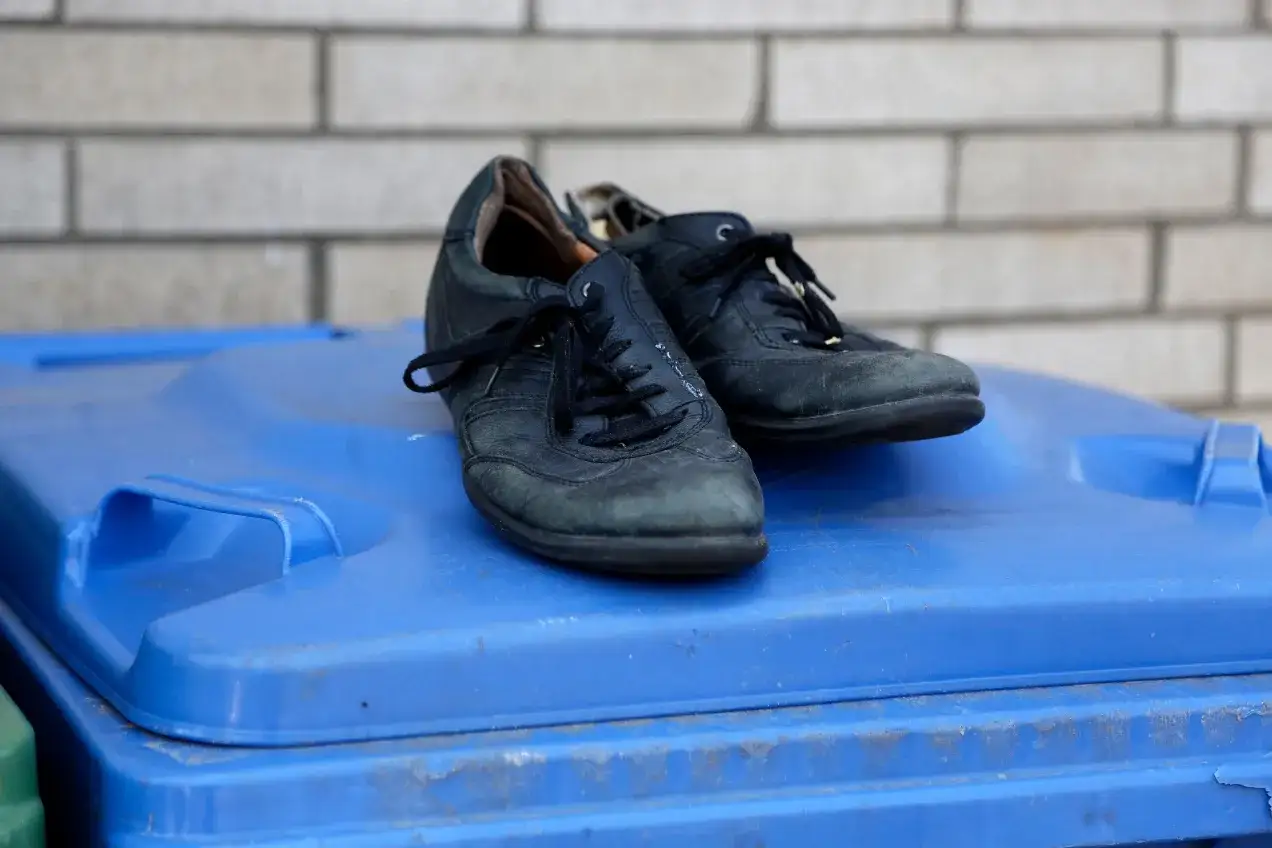 Stare czarne buty na niebieskim koszu na śmieci. Zastanawiasz się, gdzie wyrzucić buty gumowe? To nie są gumowe, ale też już zużyte.