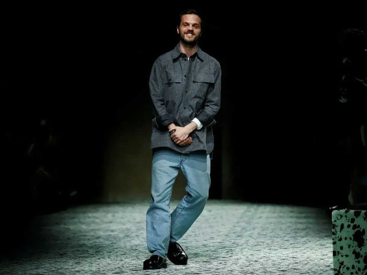 Matthieu Blazy, diseñador de Bottega Veneta, sonríe en la pasarela con camisa gris y vaqueros.